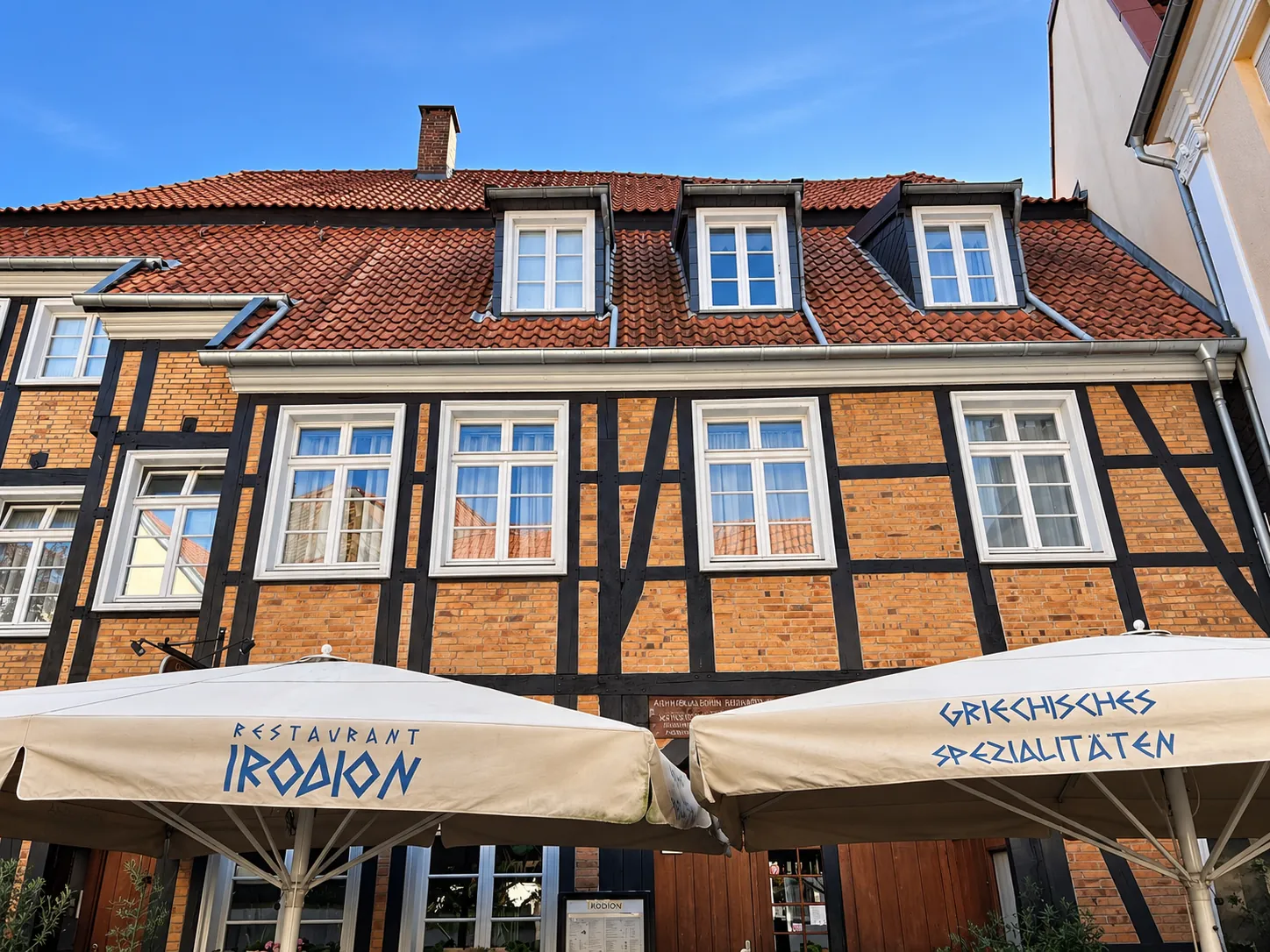 Das Fachwerkhaus am Roggenmarkt 19 in der Sonne, davor die hellen Sonnenschirme mit dem Schriftzug Restaurant Irodion.