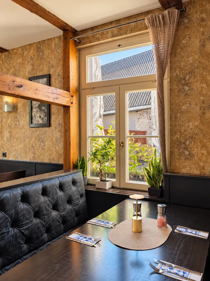 Ein Tisch in einer Fensternische an einer gepolsterten Bank, darüber ein Holzbalken.