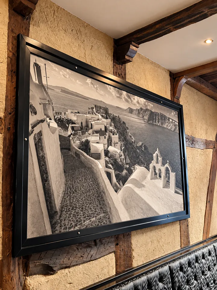 Ein großes Schwarzweißfoto von Santorini in dunklem Rahmen an der Wand über einer Polsterbank.