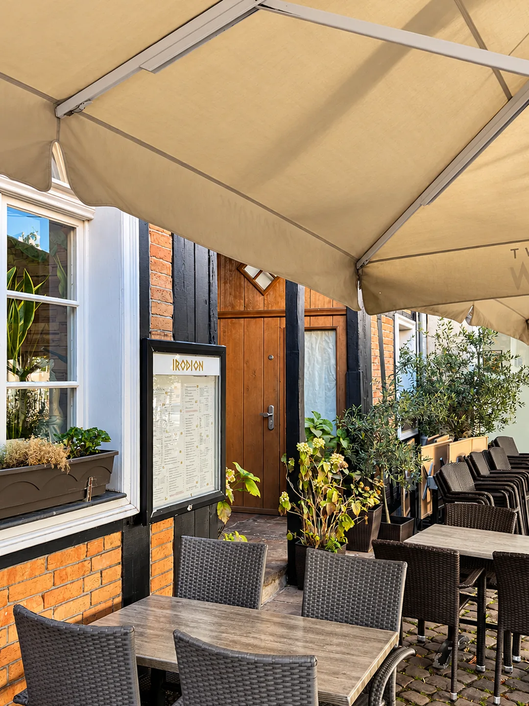 Tische auf der Terrasse unter großen Sonnenschirmen, daneben die Fachwerkwand mit der Speisekarte des Hauses.